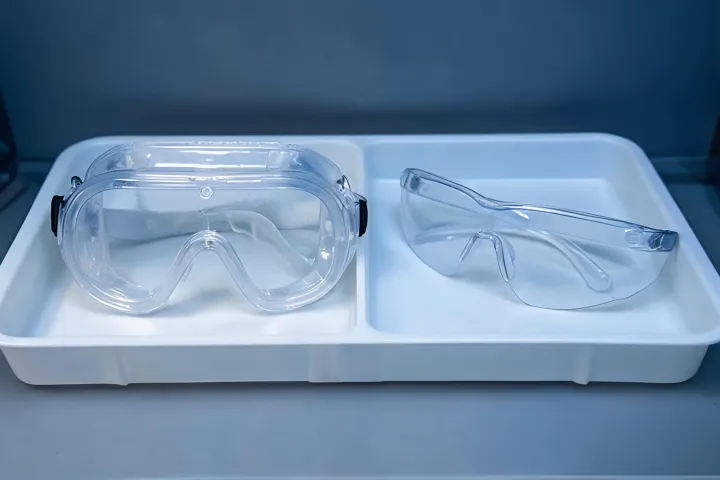 Side-by-side unlabeled splash goggles and open safety glasses on a comparison tray